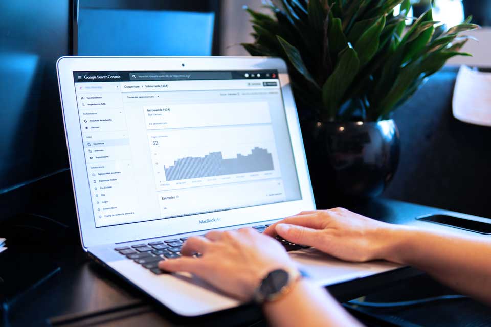 2 hands restingon a laptop keyboard, which is open at a page of Google search console to work on Local SEO monitoring. The page is open at the 404 page impressions. The laptop is resting on a small black table, which has a succulent green plant in a round black plant holder.